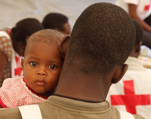 Foto: Ein haitianisches Baby schaut über die Schulder eines Rotkreuzhelfers.