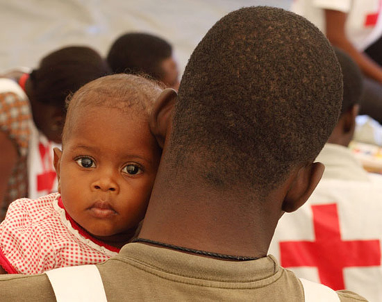 Foto: Ein haitianisches Baby schaut über die Schultern eines Rotkreuzhelfers.